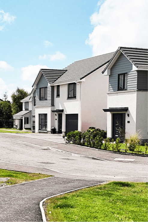 Row of modern UK new-build houses with cream render, grey cladding, and pitched tiled roofs on a quiet suburban street